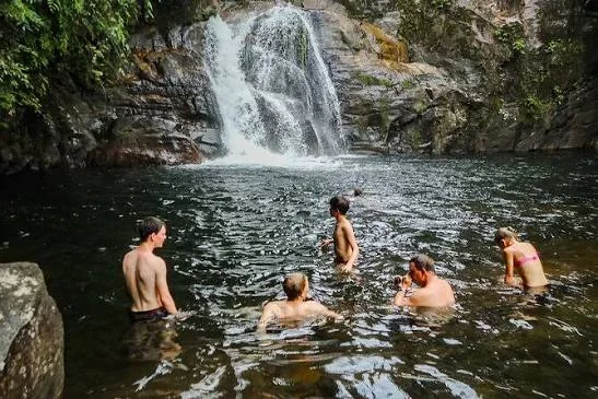 Visitors enjoying a natural pool and waterfall in Sinharaja